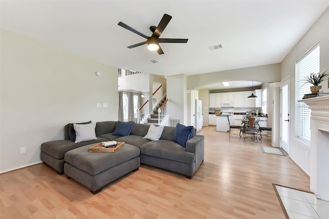 17006 Valley Palms Dr, Spring, TX 77379 - living room featuring ceiling fan, arched walkways, light wood-style flooring, stairs, and a fireplace with flush hearth
