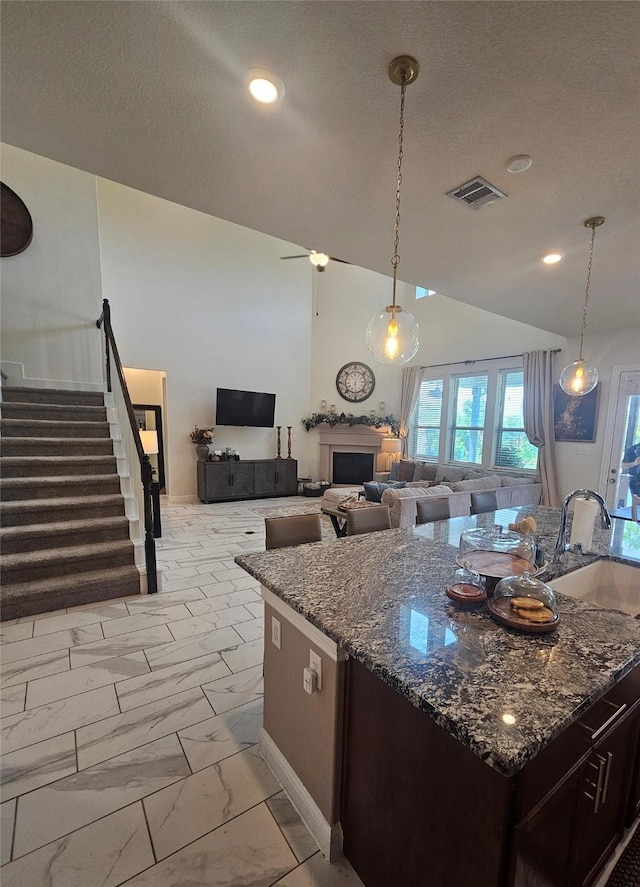 1013 Goose Creek St, Webster, TX 77598 - kitchen featuring light marble finish floors, dark stone countertops, dark brown cabinets, a fireplace, and a textured ceiling