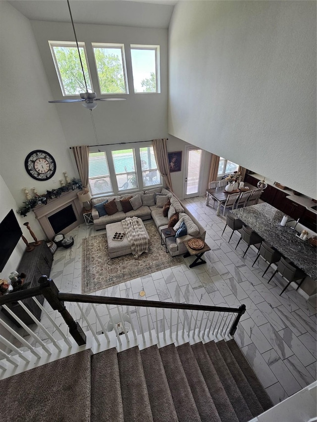 1013 Goose Creek St, Webster, TX 77598 - living room featuring a high ceiling, a ceiling fan, a fireplace, marble look tiles, and stairs