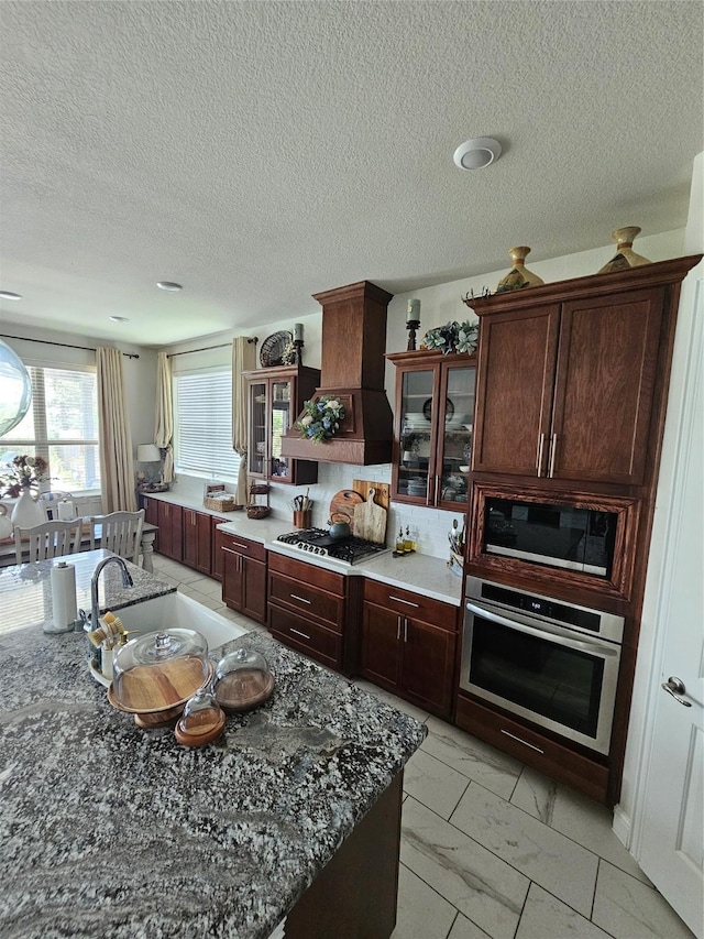 1013 Goose Creek St, Webster, TX 77598 - kitchen with appliances with stainless steel finishes, premium range hood, light marble finish floors, glass insert cabinets, and a textured ceiling