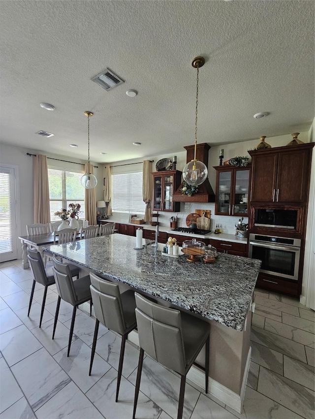 1013 Goose Creek St, Webster, TX 77598 - kitchen featuring stainless steel appliances, light marble finish floors, a breakfast bar area, glass insert cabinets, and a textured ceiling