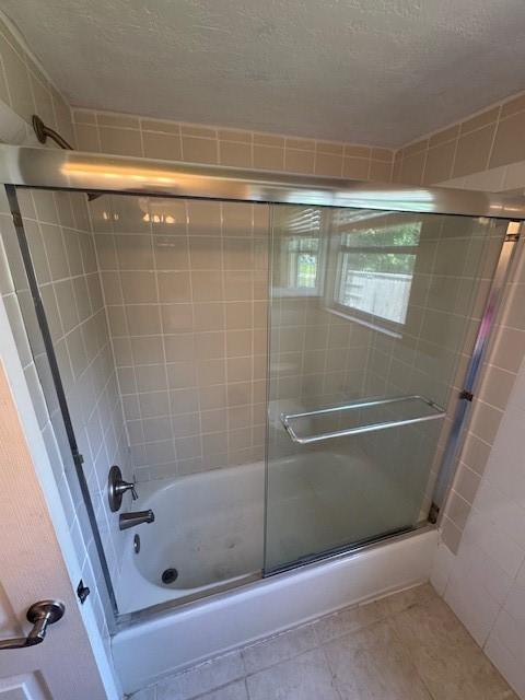 bathroom featuring a textured ceiling, enclosed tub / shower combo, and tile patterned flooring