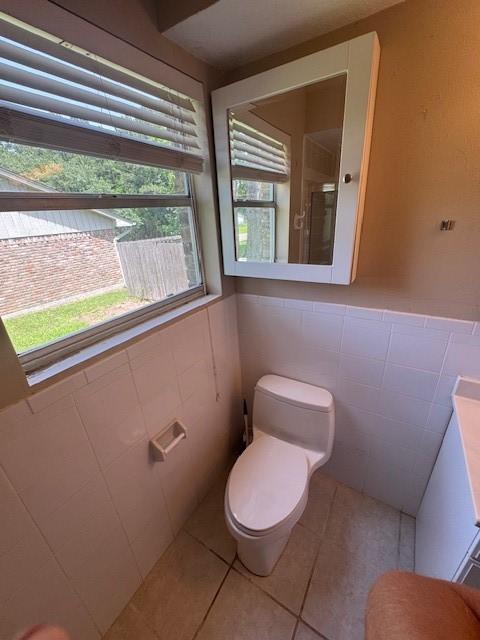 bathroom featuring tile walls, tile patterned floors, toilet, a shower with door, and wainscoting