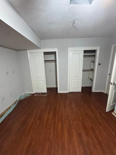 unfurnished bedroom featuring two closets, a textured ceiling, wood finished floors, and baseboards