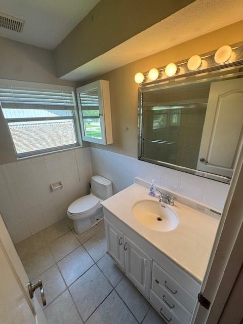 bathroom with tile walls, a stall shower, tile patterned floors, vanity, and toilet