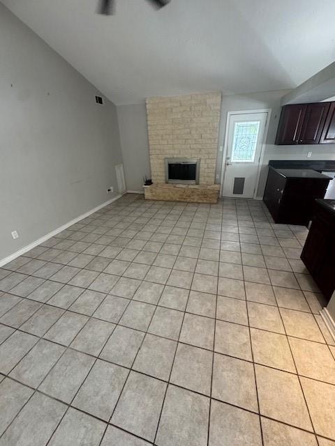 unfurnished living room featuring vaulted ceiling, a brick fireplace, light tile patterned floors, and baseboards