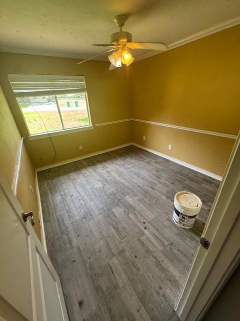 empty room with wood finished floors, crown molding, ceiling fan, and baseboards