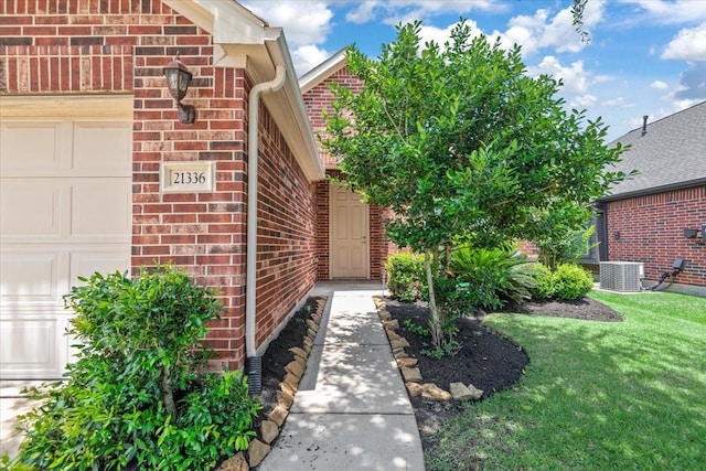doorway to property featuring brick siding, an attached garage, central AC, and a yard