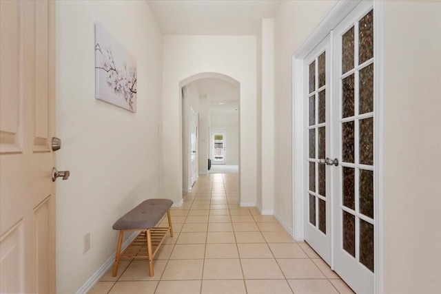 hall featuring arched walkways, french doors, light tile patterned floors, and baseboards