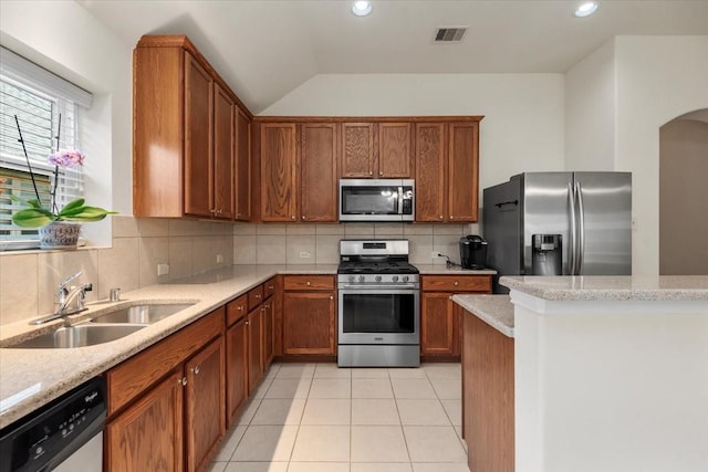 kitchen featuring stainless steel appliances, a sink, backsplash, brown cabinetry, and recessed lighting