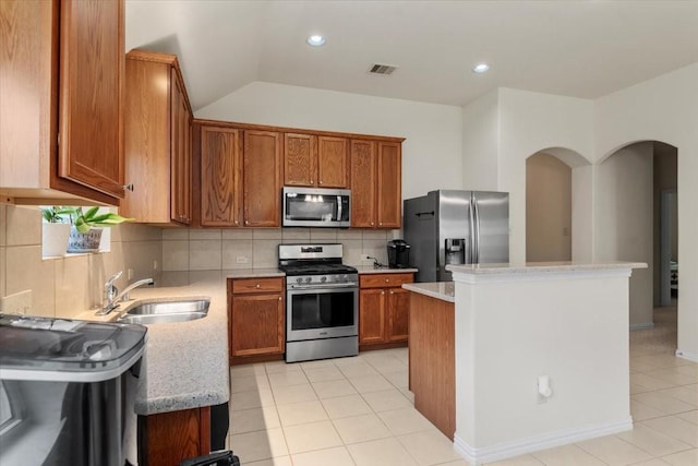 kitchen with appliances with stainless steel finishes, a sink, a center island, backsplash, and brown cabinets