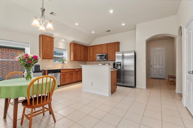 kitchen featuring appliances with stainless steel finishes, arched walkways, tasteful backsplash, brown cabinets, and light countertops