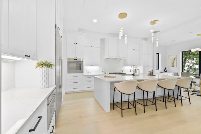 5115 Maple St, Houston, TX 77401 - kitchen featuring appliances with stainless steel finishes, light wood-type flooring, a breakfast bar area, an island with sink, and white cabinets