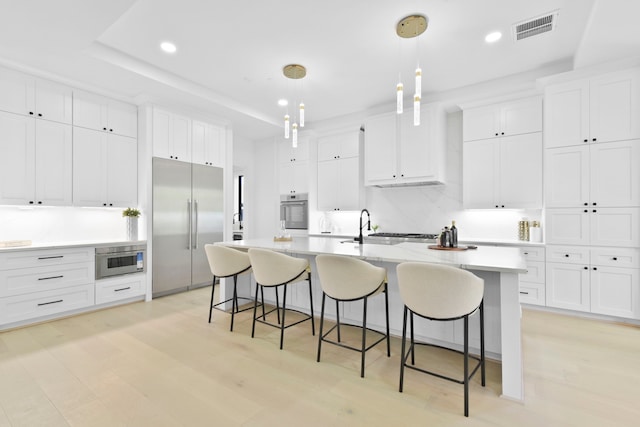 5115 Maple St, Houston, TX 77401 - kitchen with stainless steel appliances, white cabinets, a kitchen island with sink, light wood-style floors, and a kitchen bar