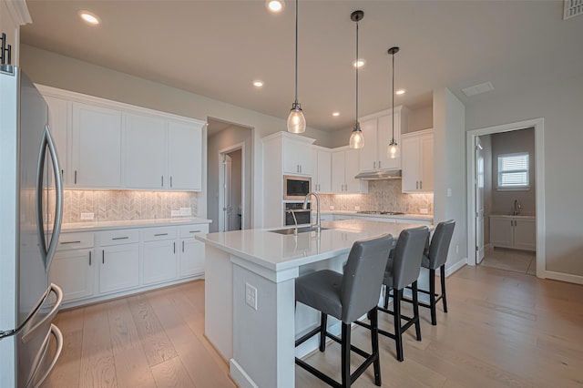 21714 Jenolan Ridge Rd, Cypress, TX 77433 - kitchen featuring stainless steel appliances, backsplash, light wood-style floors, an island with sink, and white cabinetry