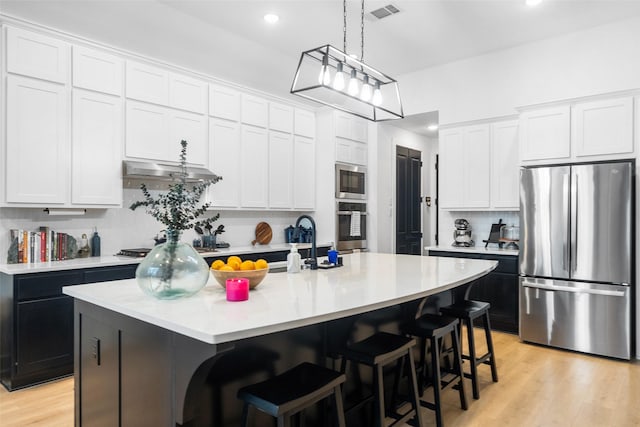 15040 Berry Brook Dr, Conroe, TX 77302 - kitchen featuring appliances with stainless steel finishes, light countertops, backsplash, a kitchen bar, and light wood-type flooring