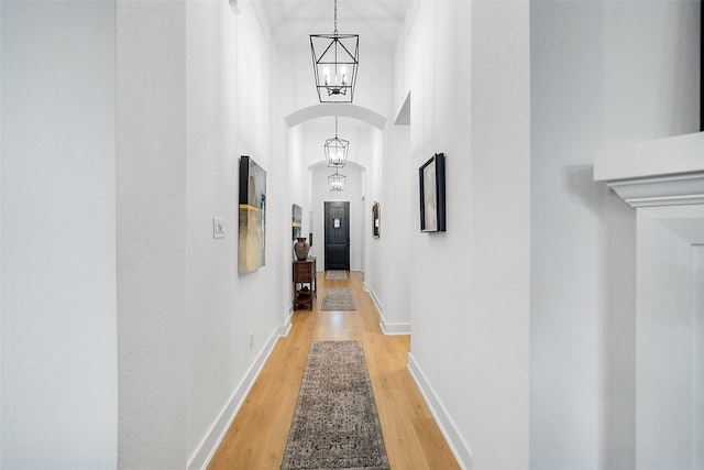 15040 Berry Brook Dr, Conroe, TX 77302 - hall featuring arched walkways, light wood finished floors, a chandelier, baseboards, and a towering ceiling