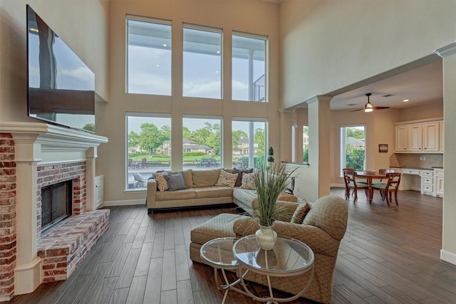 11872 Seashell Cir, Montgomery, TX 77356 - living room featuring dark wood-style floors, a high ceiling, ceiling fan, a brick fireplace, and baseboards