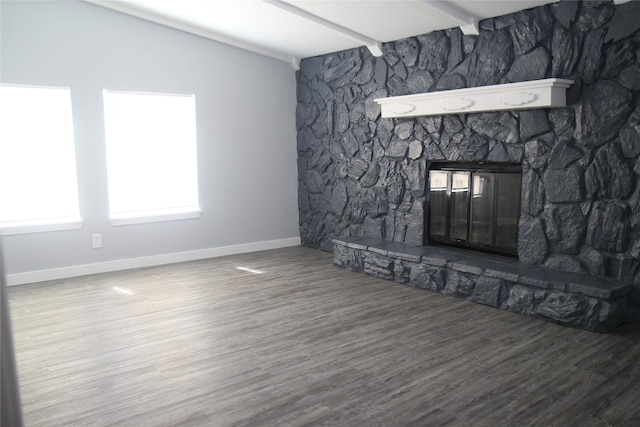 unfurnished living room with a stone fireplace, wood finished floors, beam ceiling, and baseboards