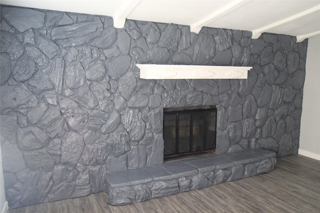detailed view of beamed ceiling, a stone fireplace, wood finished floors, and baseboards