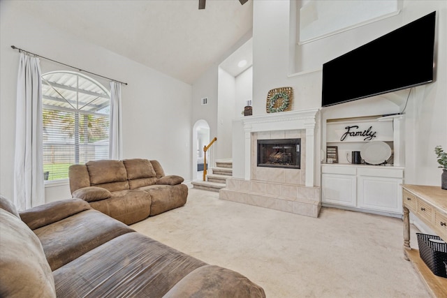 3413 Somerset Ln, Deer Park, TX 77536 - living room featuring light carpet, high vaulted ceiling, arched walkways, a tile fireplace, and stairs
