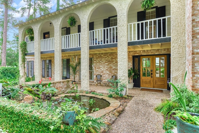 doorway to property featuring a balcony, french doors, and brick siding