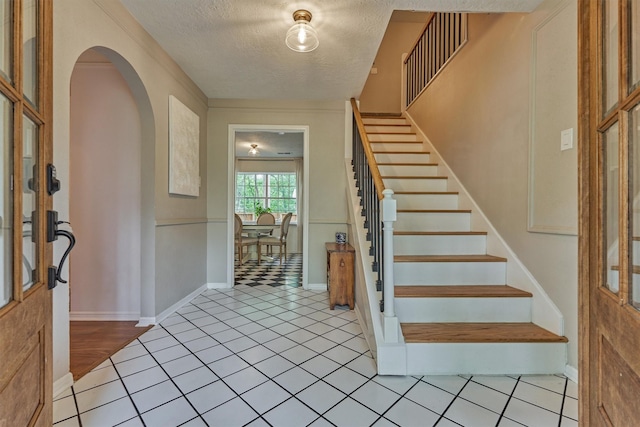 entrance foyer featuring arched walkways, a textured ceiling, stairs, tile patterned flooring, and baseboards