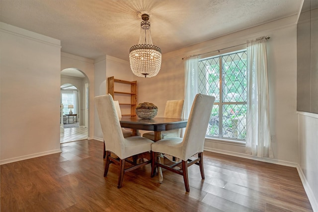 dining space featuring arched walkways, a chandelier, plenty of natural light, wood finished floors, and a textured ceiling