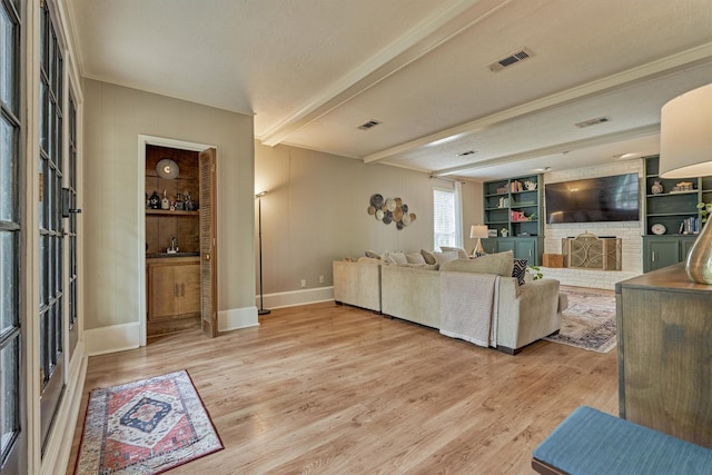living room featuring light wood-type flooring, beamed ceiling, a brick fireplace, baseboards, and ornamental molding