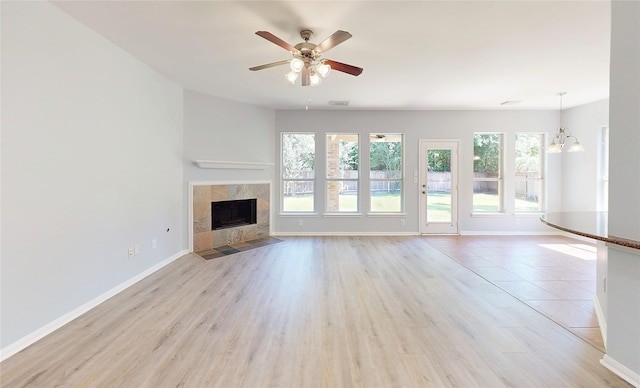 unfurnished living room featuring a ceiling fan, light wood-type flooring, a tiled fireplace, and baseboards