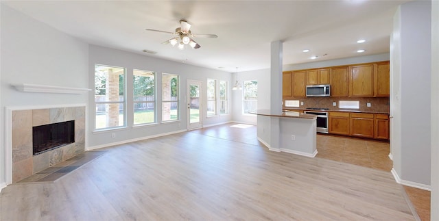 kitchen with stainless steel microwave, stove, open floor plan, ceiling fan, and decorative backsplash