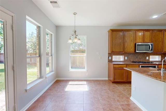 kitchen featuring stainless steel microwave, light stone counters, brown cabinetry, backsplash, and recessed lighting