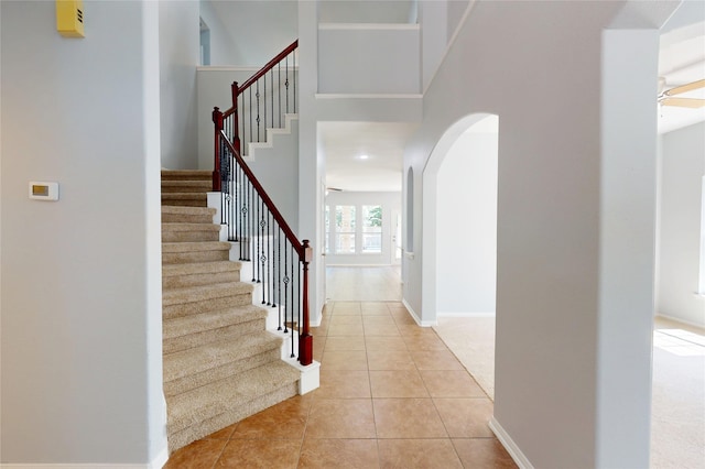 foyer entrance featuring arched walkways, stairway, light tile patterned floors, baseboards, and a high ceiling
