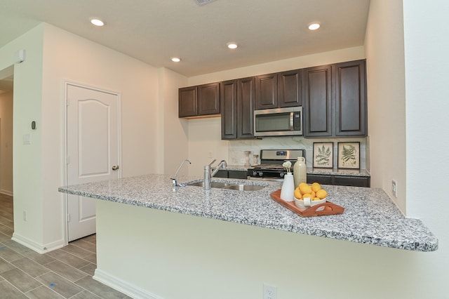 27638 Mesabe Dr, Magnolia, TX 77354 - kitchen with appliances with stainless steel finishes, a sink, dark brown cabinetry, baseboards, and light stone counters