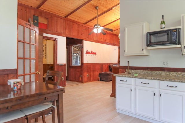 302 Bluebonnet Rd, Sheridan, TX 78950 - kitchen with black microwave, wooden walls, wood ceiling, white cabinetry, and a wainscoted wall