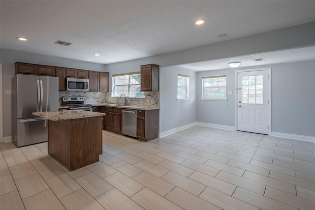 1109 Dismuke St, Houston, TX 77023 - kitchen featuring stainless steel appliances, baseboards, decorative backsplash, light stone counters, and a kitchen island