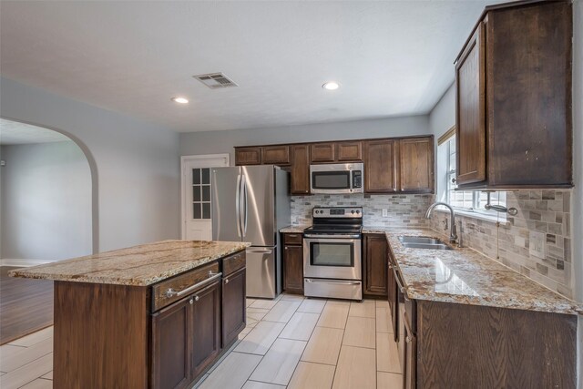 1109 Dismuke St, Houston, TX 77023 - kitchen with appliances with stainless steel finishes, arched walkways, a sink, tasteful backsplash, and light stone counters
