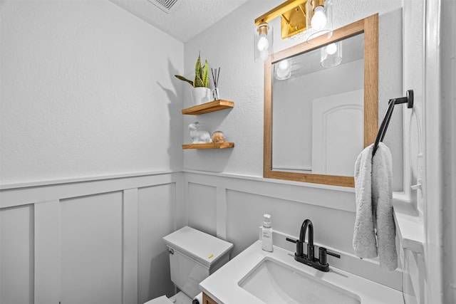 5702 W Vistaglen Loop, Houston, TX 77084 - bathroom with toilet, a decorative wall, vanity, a wainscoted wall, and a textured ceiling
