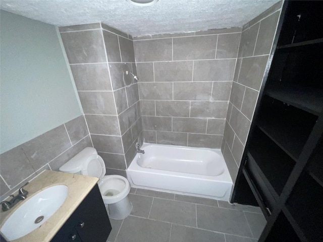 745 Yorkshire St, Houston, TX 77022 - full bathroom with tile walls, a textured ceiling, toilet, tile patterned floors, and bathing tub / shower combination