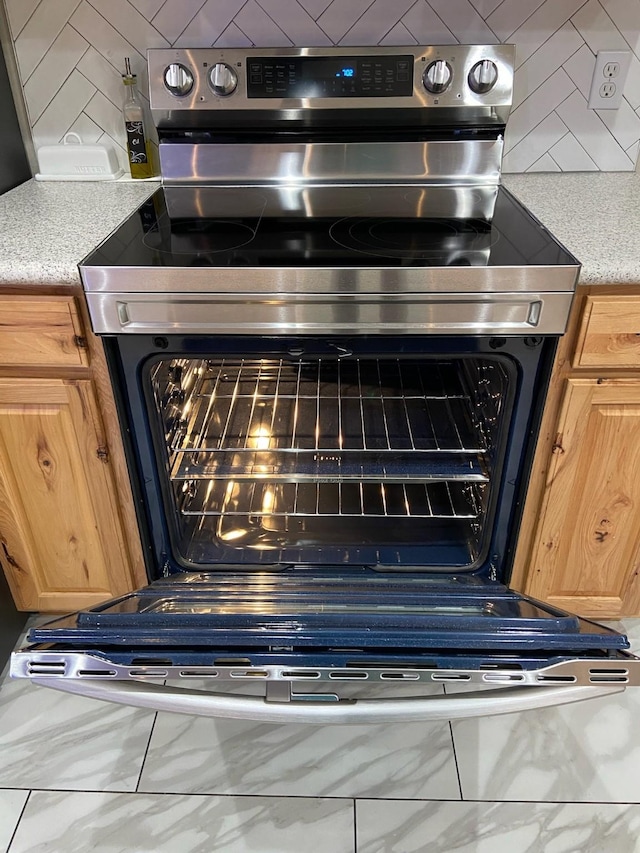 195 Rim Rock Rd, Onalaska, TX 77360 - kitchen view of stainless steel range with electric stovetop, backsplash, light countertops, and light brown cabinetry
