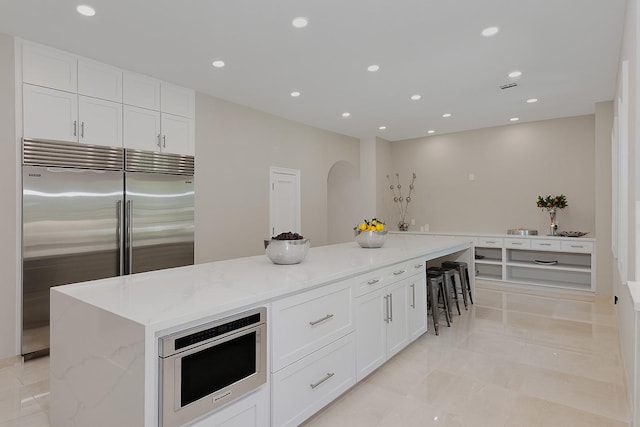 kitchen featuring stainless steel built in refrigerator, light stone counters, white cabinets, recessed lighting, and a spacious island