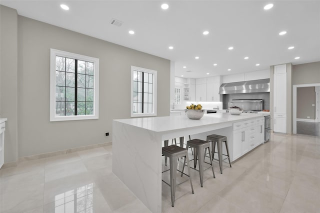 kitchen with white cabinets, exhaust hood, recessed lighting, light countertops, and a breakfast bar