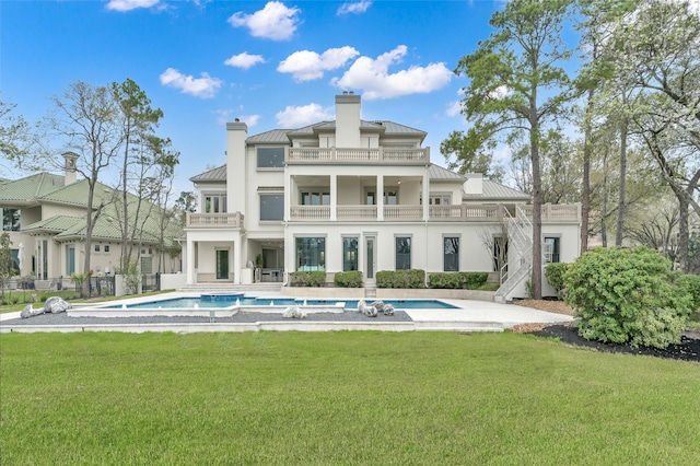 back of property with a standing seam roof, a balcony, an outdoor pool, and a lawn