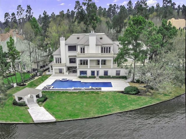 rear view of property featuring a balcony, a chimney, a gazebo, a lawn, and a water view