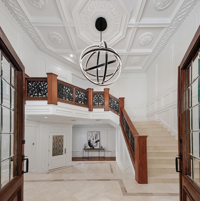 foyer with a decorative wall, inlaid floor details, stairs, a chandelier, and a high ceiling