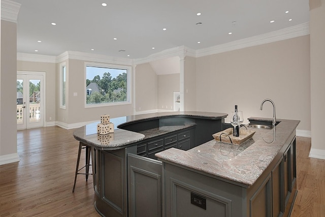 kitchen with a center island with sink, open floor plan, a sink, light stone counters, and ornamental molding