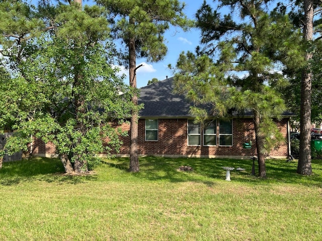 view of front of home featuring roof with shingles, a front lawn, and brick siding