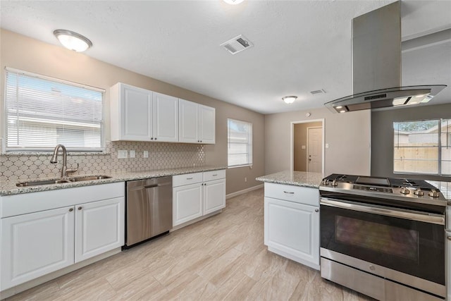 9314 Kristin Dr, Houston, TX 77031 - kitchen featuring appliances with stainless steel finishes, a sink, island exhaust hood, white cabinetry, and decorative backsplash