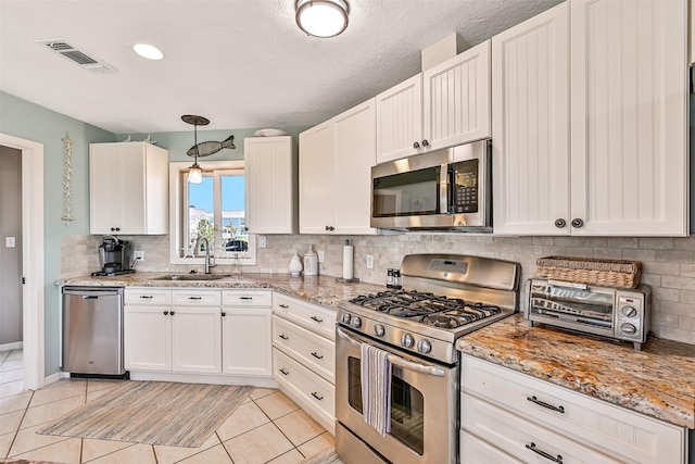 kitchen featuring appliances with stainless steel finishes, a sink, light tile patterned flooring, backsplash, and white cabinets