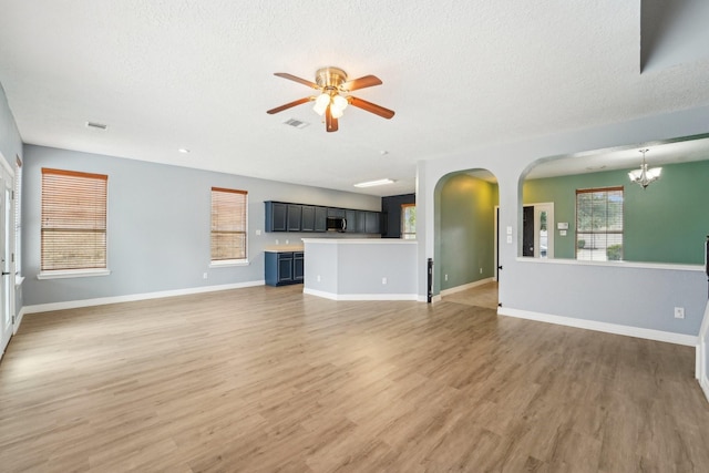 3339 Legends Creek Dr, Spring, TX 77386 - unfurnished living room with a ceiling fan, a chandelier, arched walkways, light wood-style floors, and a textured ceiling